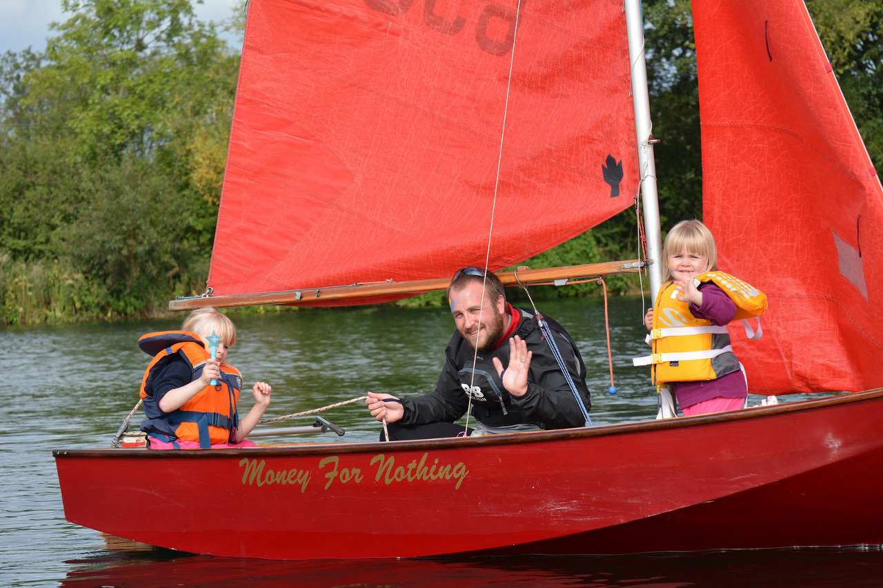 A red Mirror dinghy racing with two children crewing