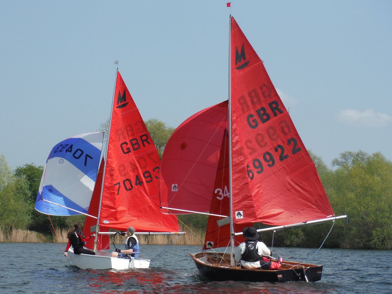 Two Mirror dinghies racing downwind on a lake with spinnakers set