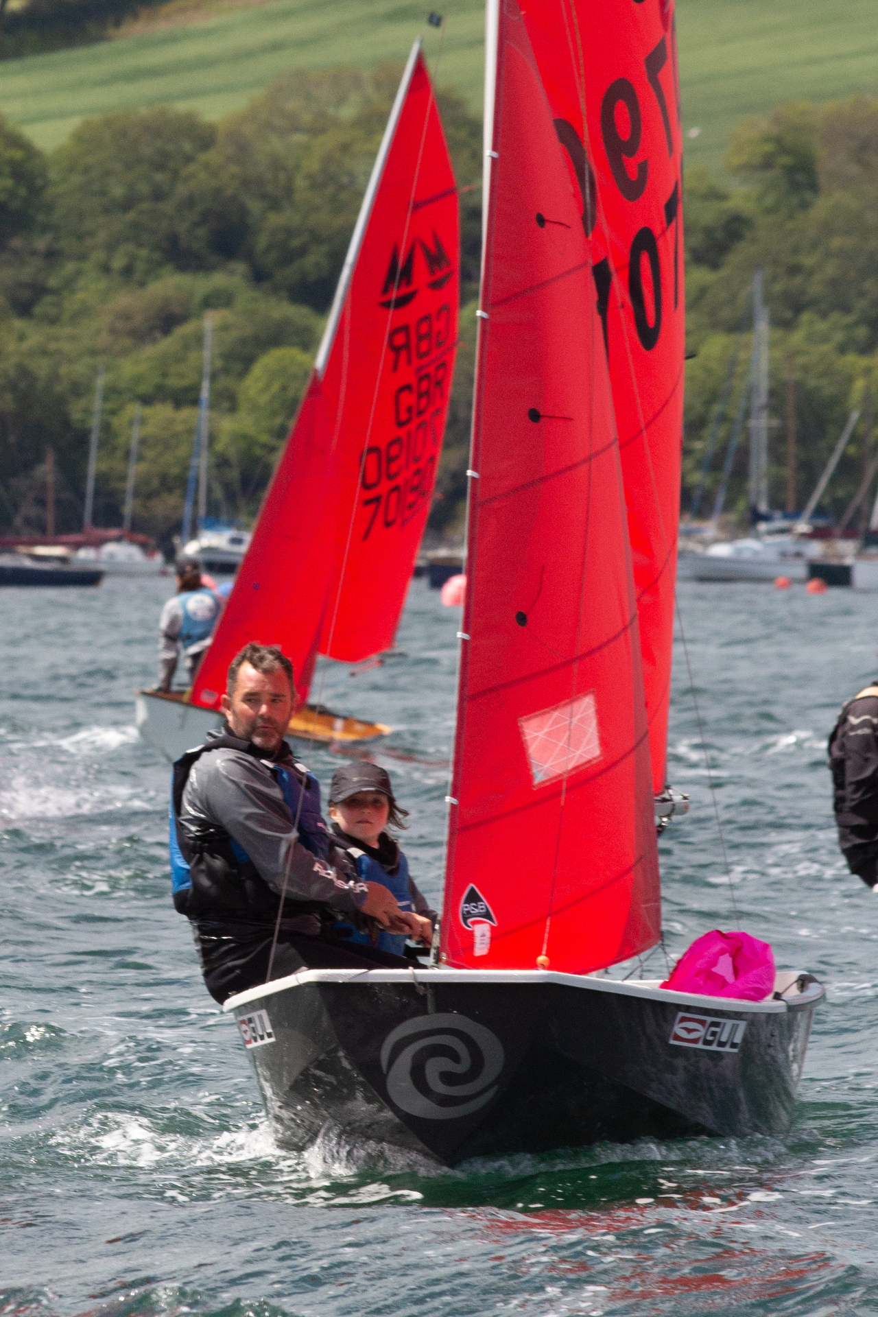 A grey Mirror dinghy being steered by an eight year old girl with dad crewing, approaching the windward mark on starboard tack
