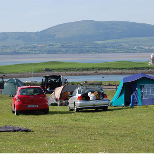 A campsite with tents, cars & vans with an estuary and hills in the background