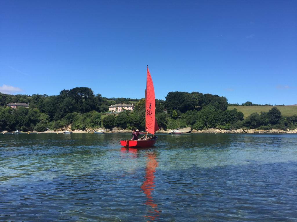 A red wooden Mirror dinghy sailing in inlet of the Carrick Roads on a sunny day