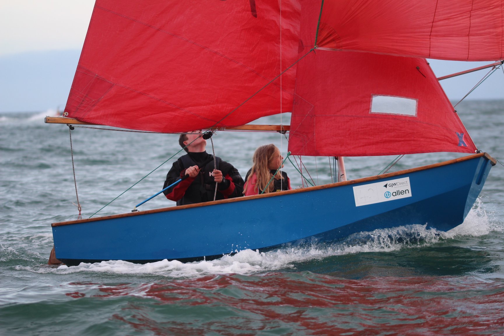 A blue wooden Mirror dinghy racing with spinnaker set with camera to leeward
