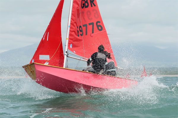 Pink wooden Mirror dinghy almost airborne in a big wave