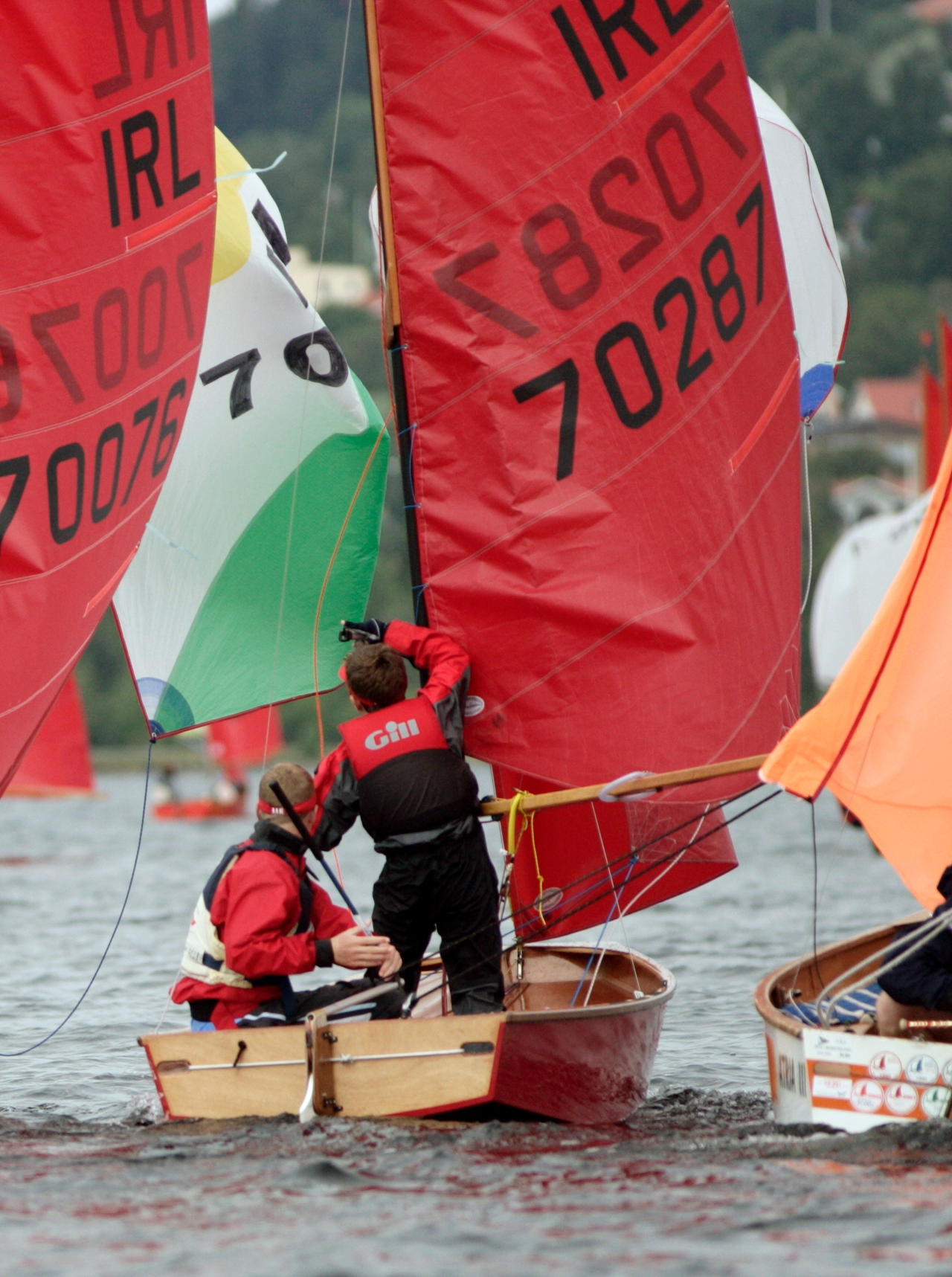 A red wooden Mirror dinghy rounding a gybe mark with a bunch of others