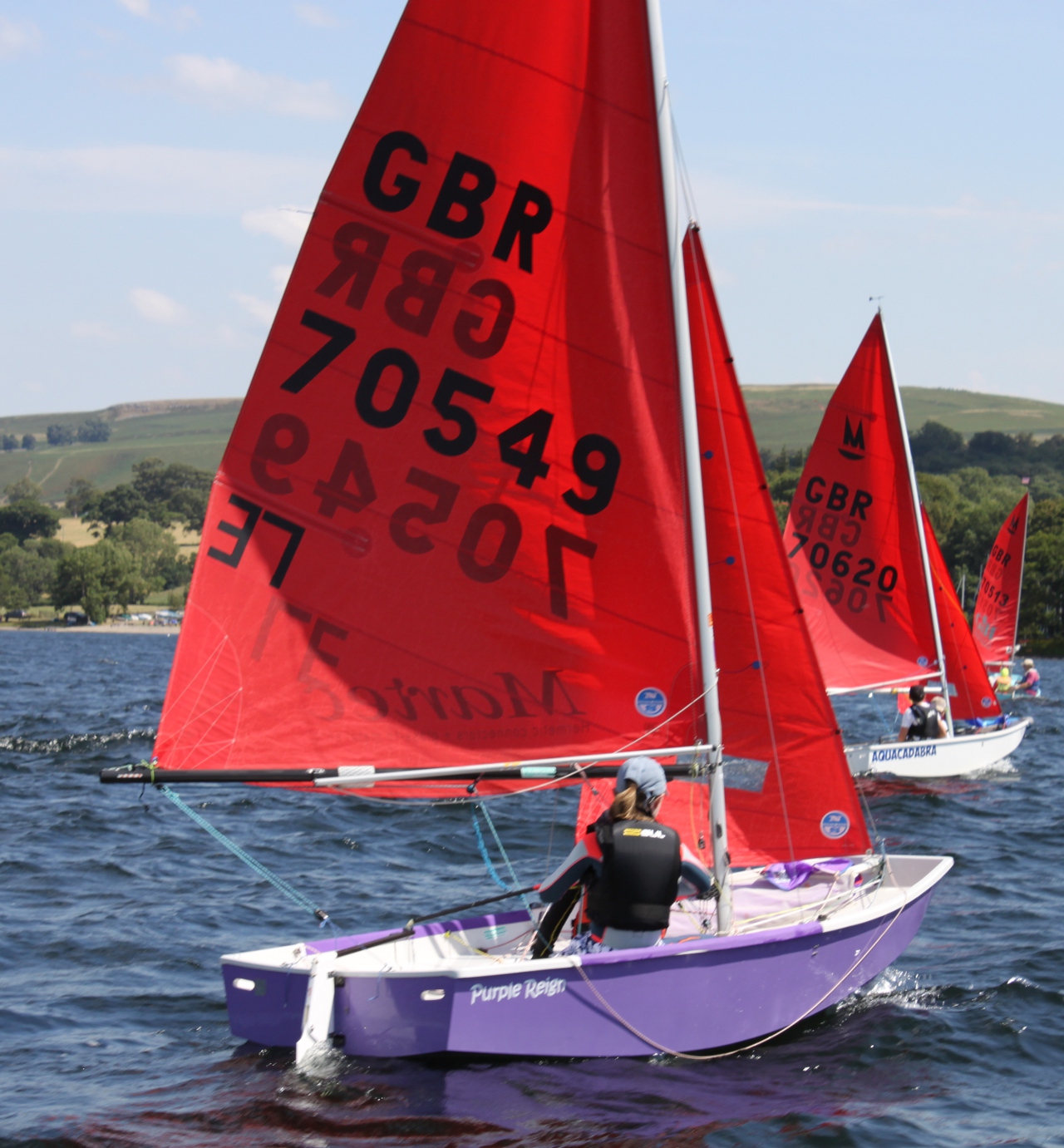A purple and white GRP Mirror dinghy racing on a lake in a moderate wind