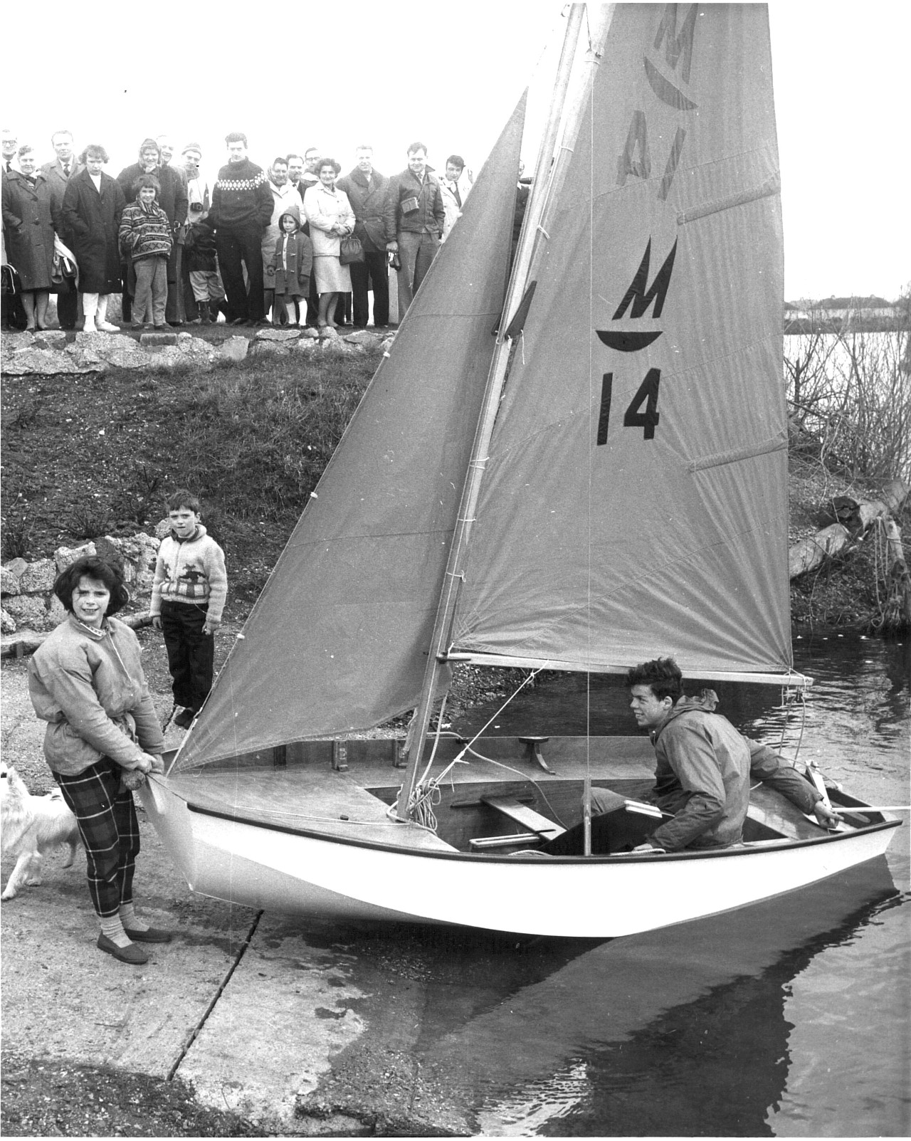 A white wooden Mirror dinghy, number 14, being held by the bow by a girl with the helm still aboard