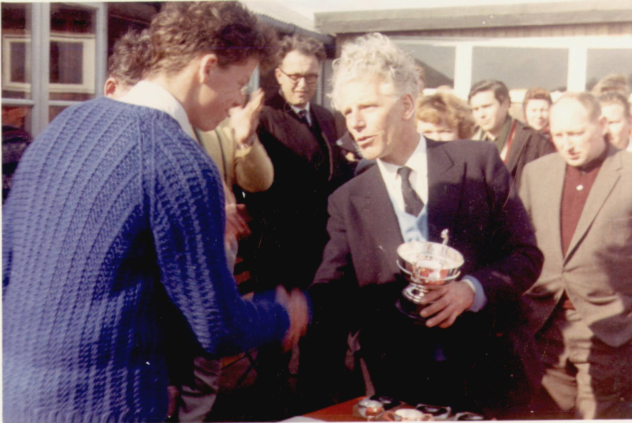 A young man collecting a trophy of a silver cup from a white haired gentleman
