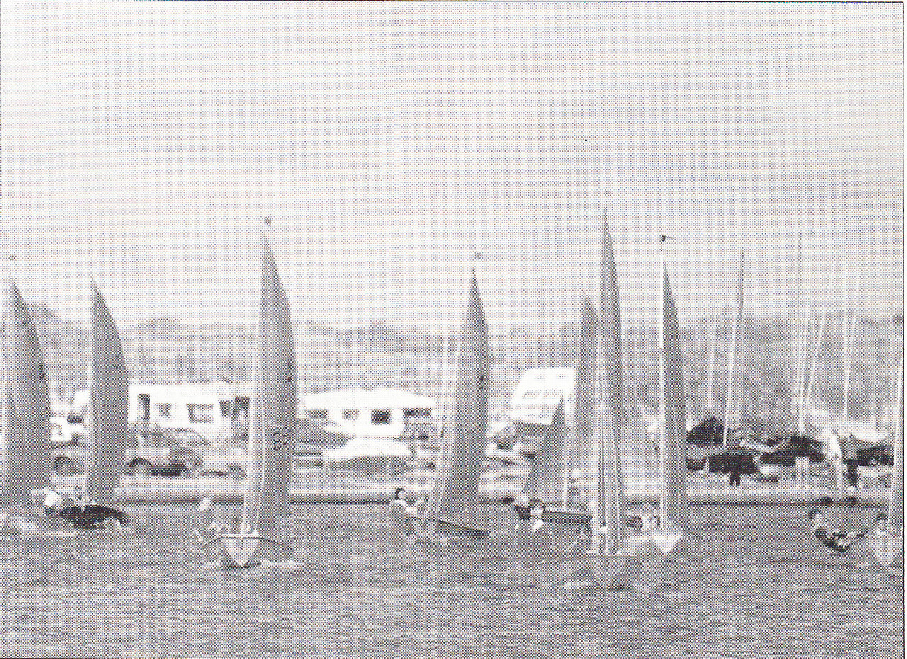 A fleet of Mirror dinghies racing to windward towards the camera in a moderate wind