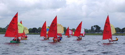 A fleet of Mirror dinghies racing on a run with spinnakers set sailing away from the camera