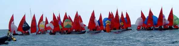 A fleet of Mirror dinghies tightly packed going around the leeward mark in light airs