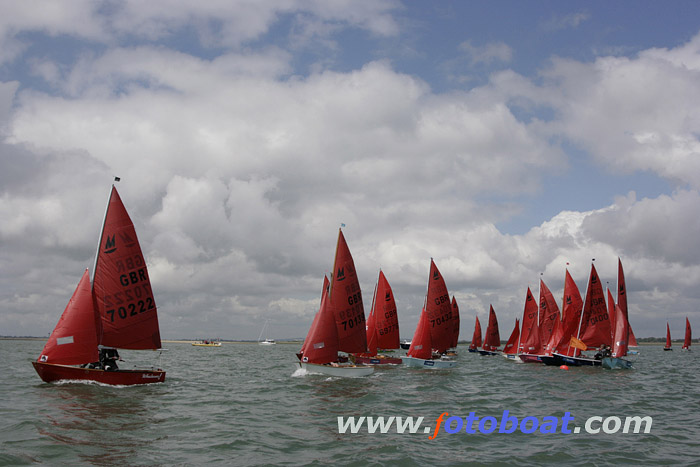 A red wooden Mirror leads the fleet away from the start line on a sunny day