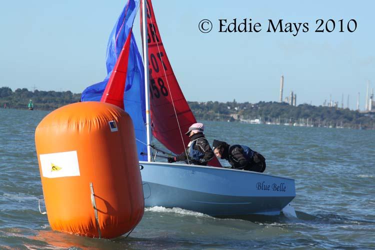 A blue Mirror dinghy dropping her spinnaker with the large orange inflatable leeward mark in the foreground