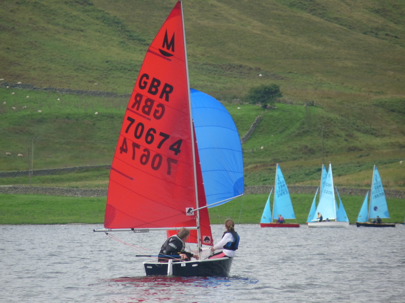 A Mirror dinghy racing downwind with spinnaker set with Enterprise dinghies in the background