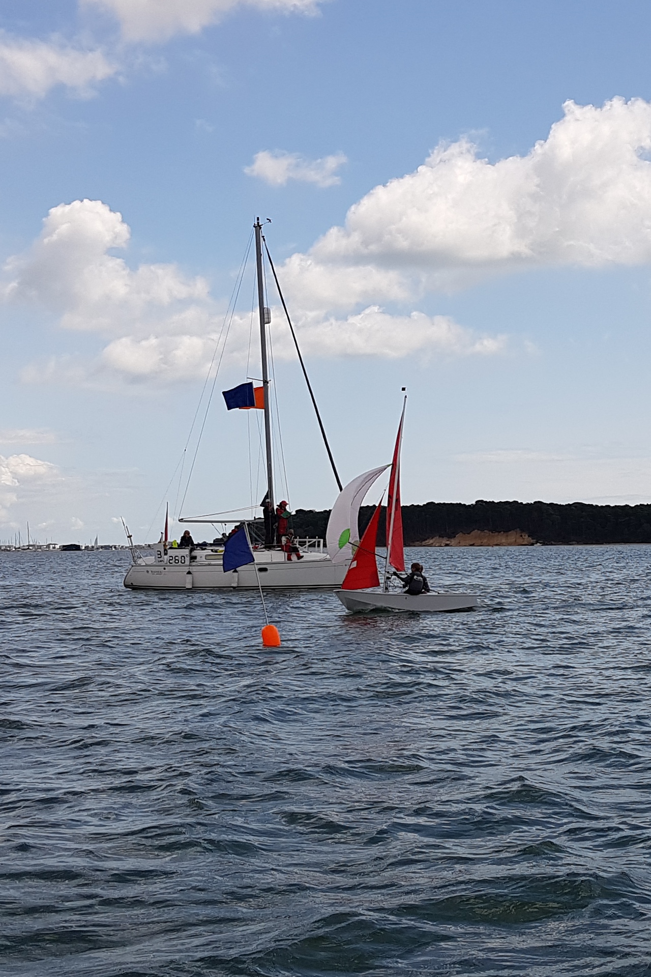 A grey GRP Mirror dinghy, with white decks crossing the finish line with spinnaker set in a light breeze