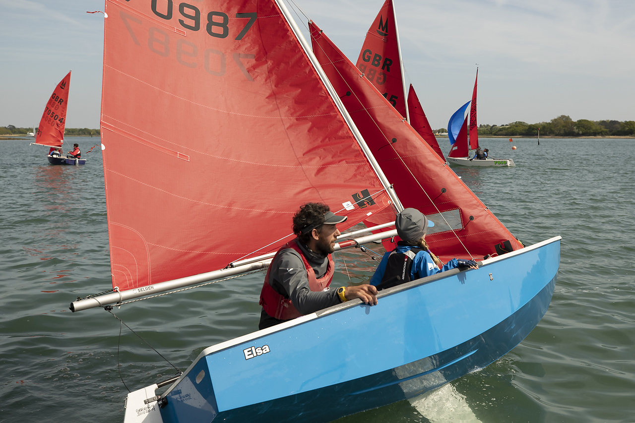 A light blue GRP Mirror dinghy roll tacking in a light wind