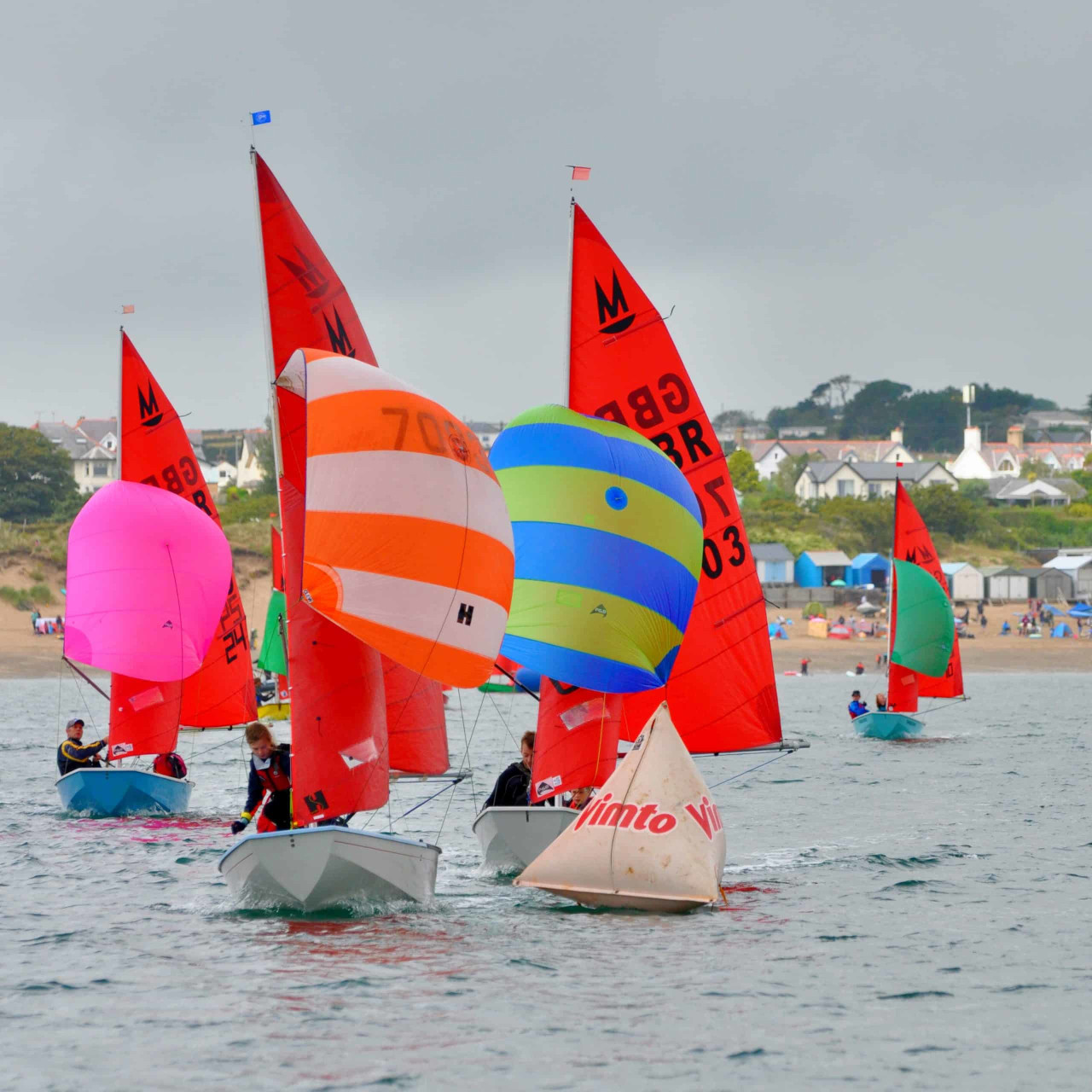 A fleet of Mirror dinghies racing downwind with spinnakers set towards a race mark in the foreground