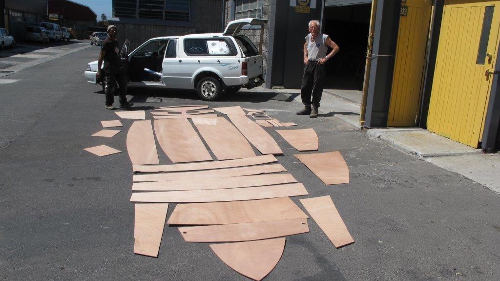 A kit of wooden plywood parts for a Mirror dinghy laid out in a car park