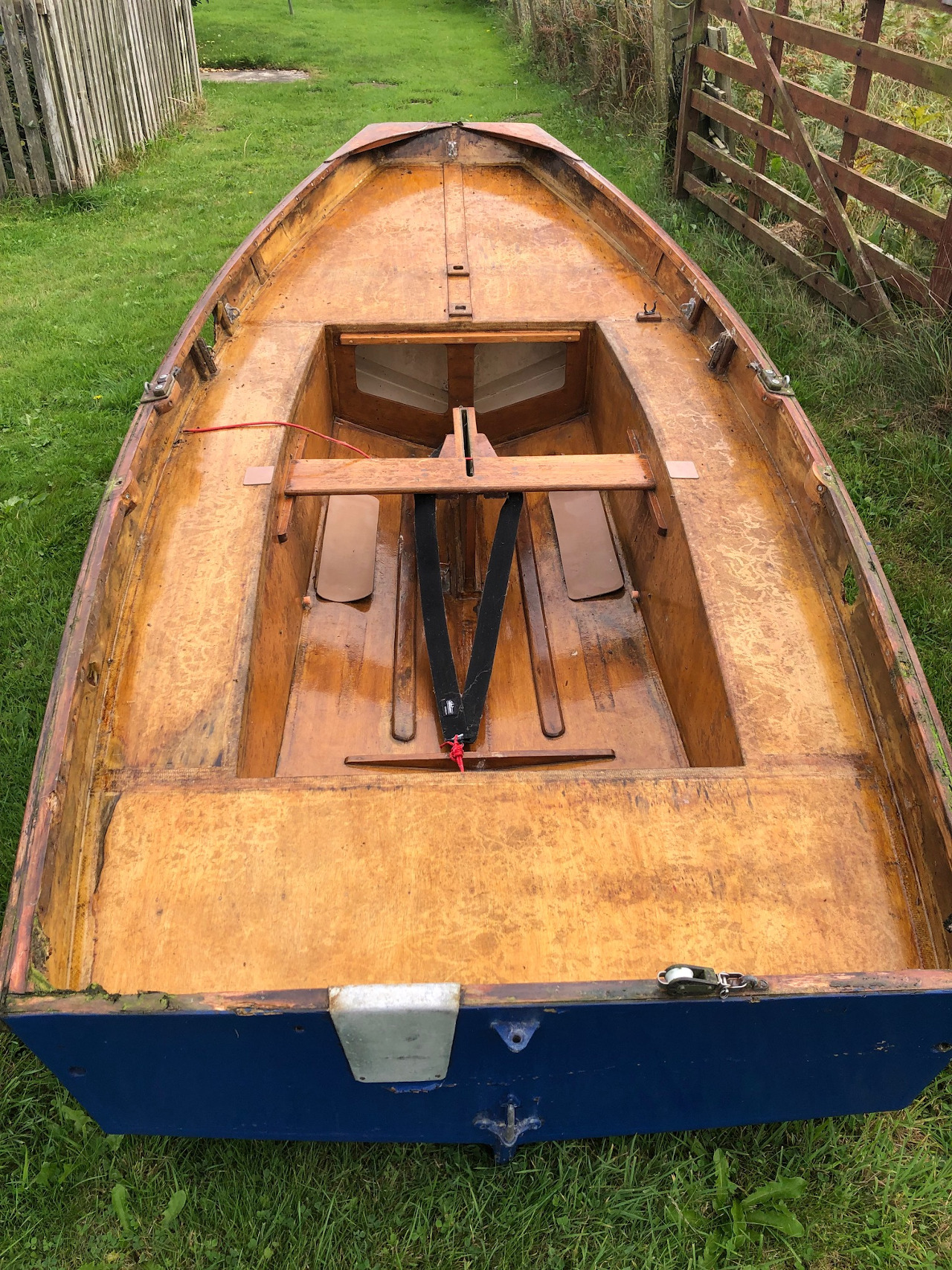 An old blue wooden Mirror dinghy hull with a small hole in the topsides in a garden 