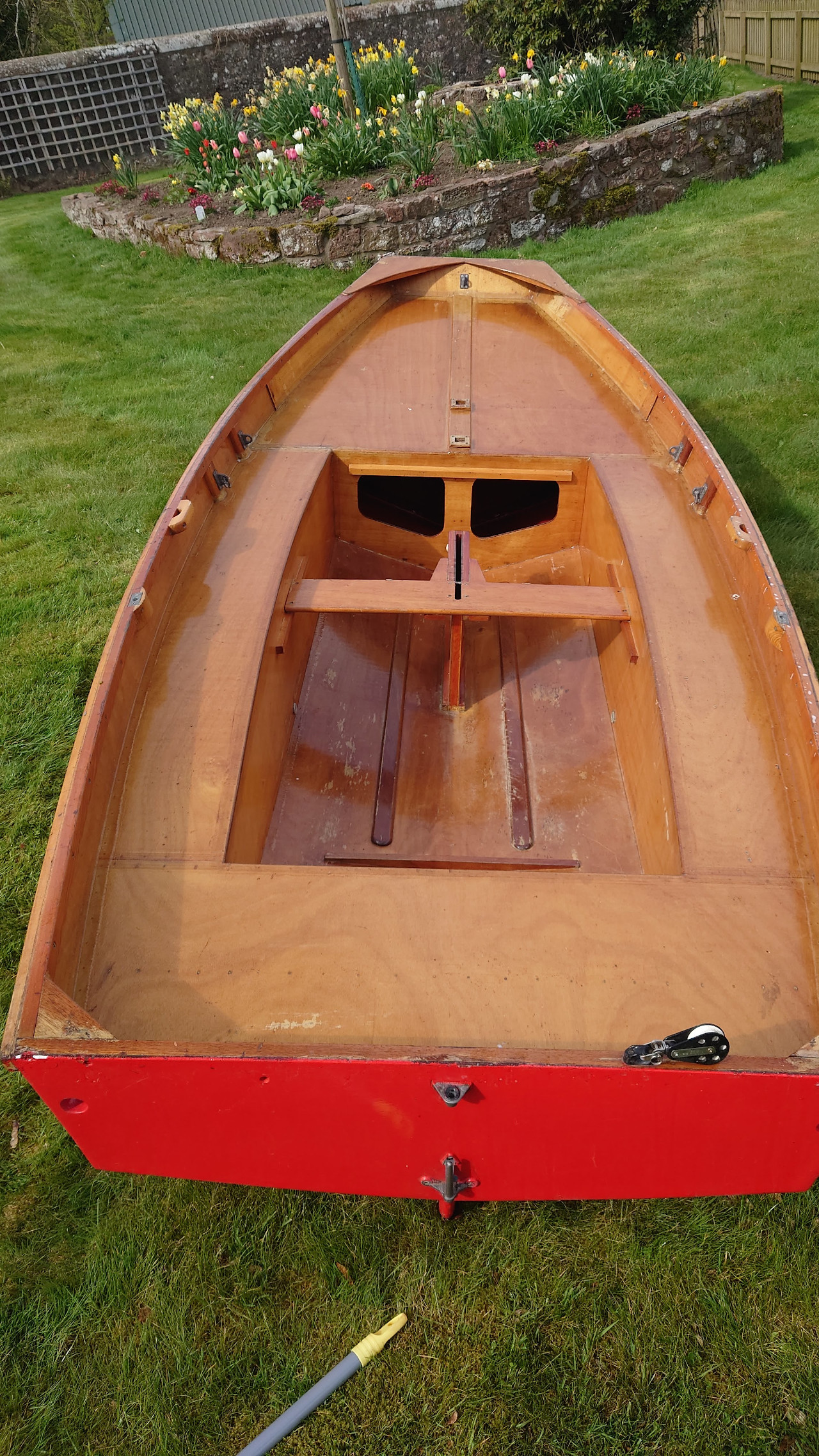 The hull of a wooden Mirror dinghy, the correct way up, on a grass lawn