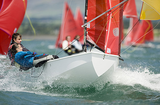 A white Mirror dinghy sailing very fast on a reach with spinnaker set, helm & crew hiking hard