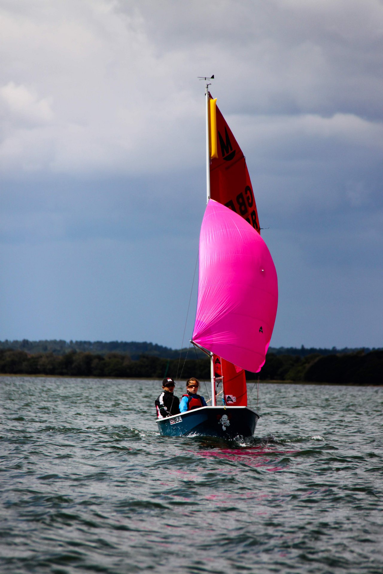 A blue and white GRP Mirror racing towards the camera with spinnaker set
