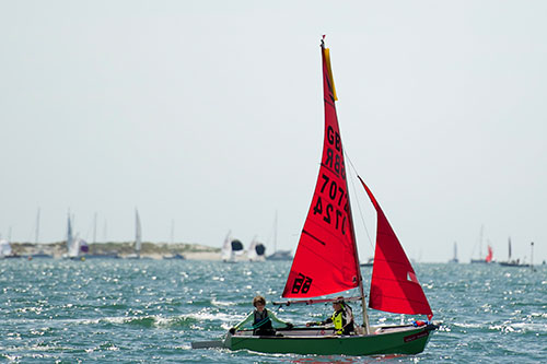 A green GRP Mirror dinghy being sailed in the distance with the rudder up