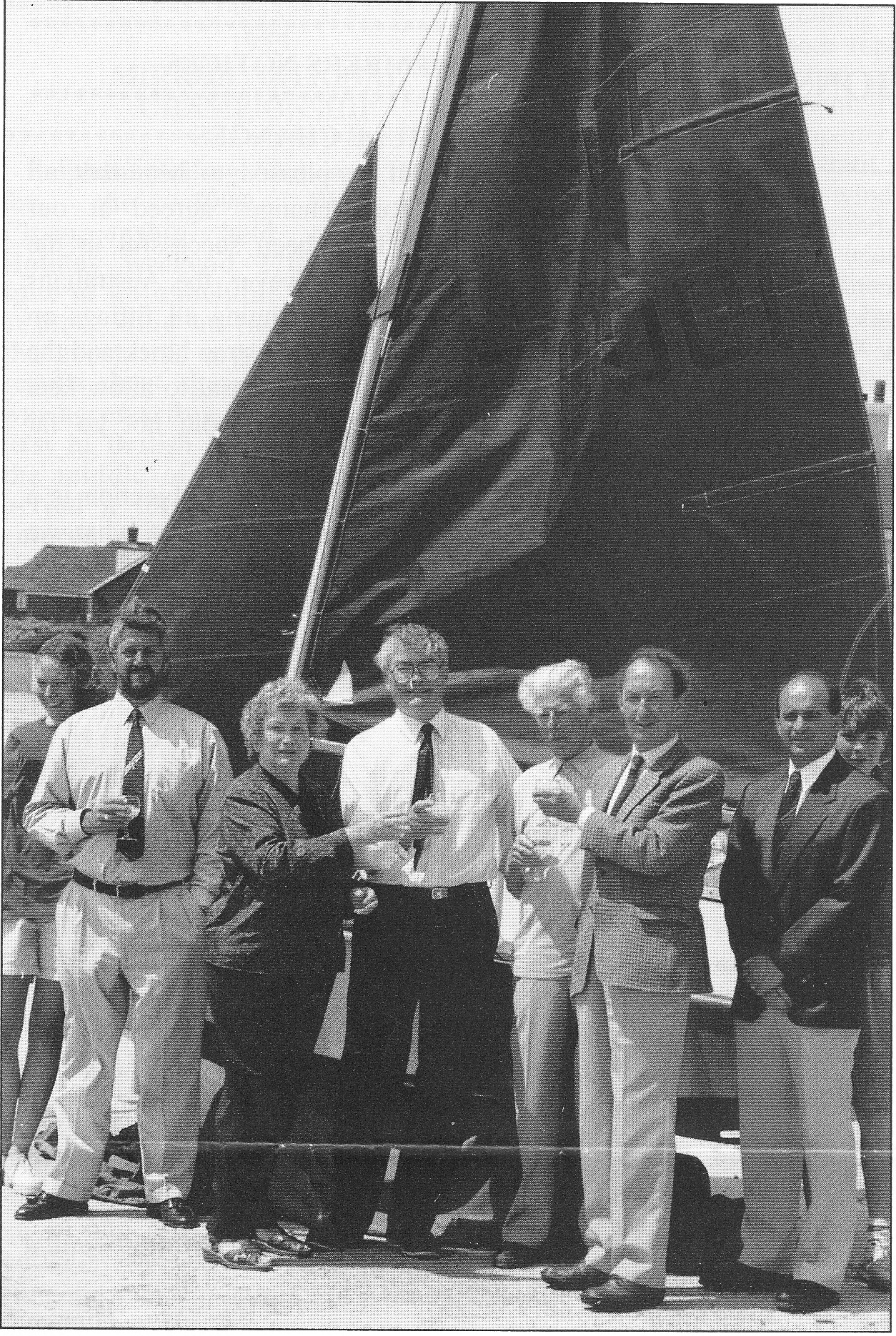 A presentation party of 8 people with a Mirror dinghy in the background